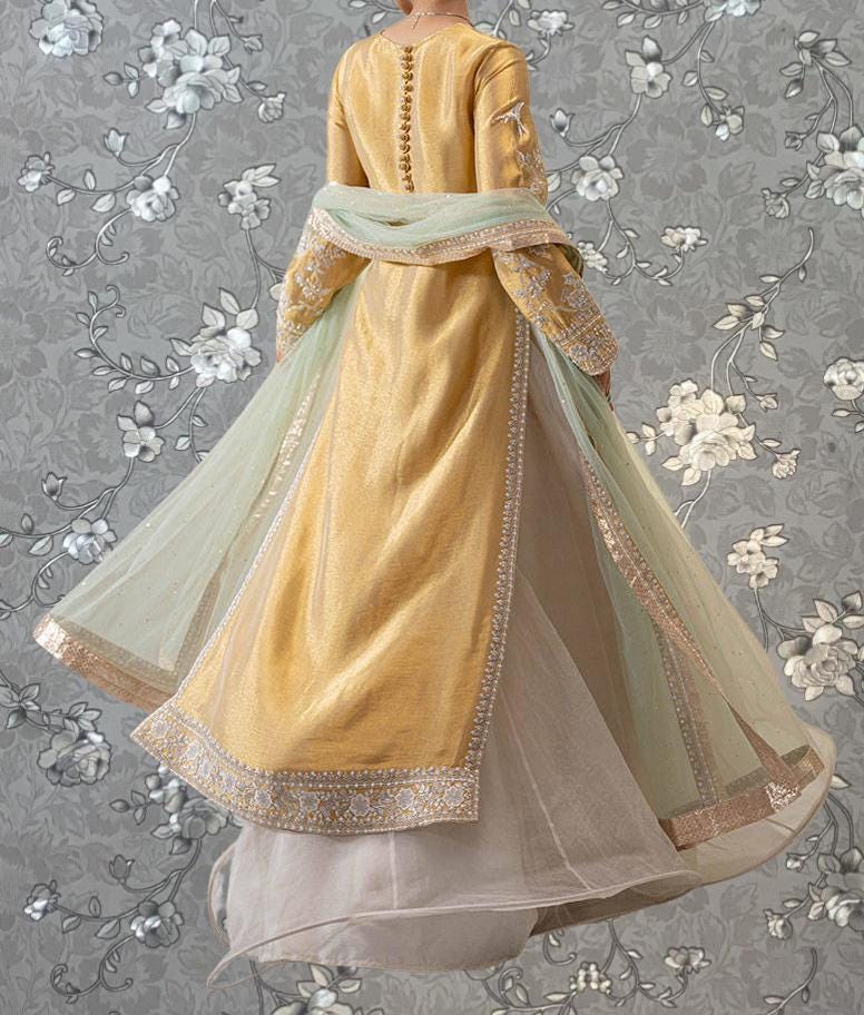 A gold and green dress with intricate embroidery and a flowing skirt is displayed against a gray floral background.