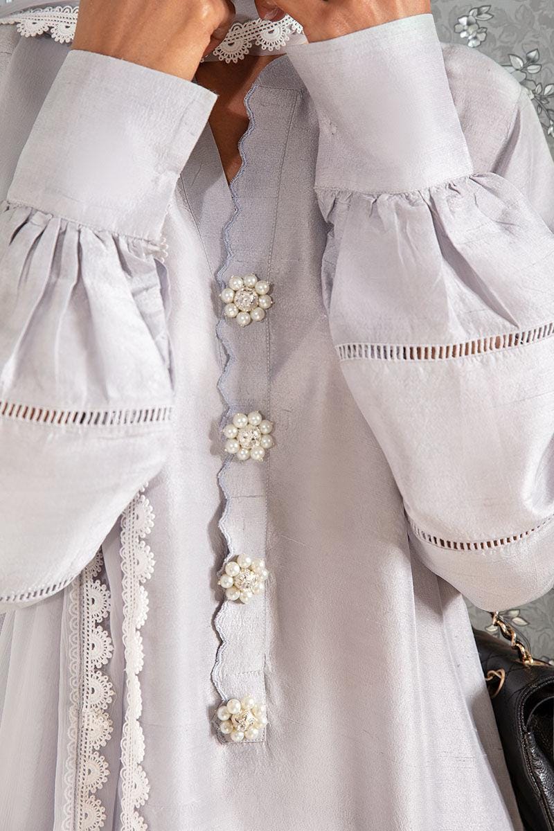A close-up view of a person wearing a white dress with intricate lace detailing and pearl buttons.