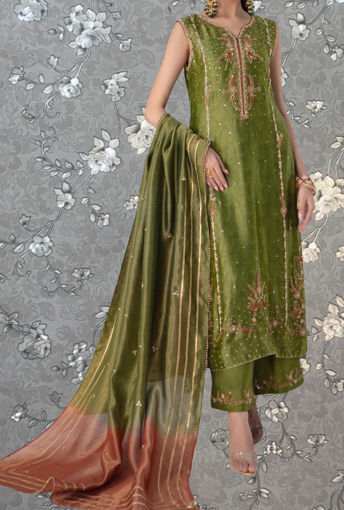 A woman wearing a green and gold dress with a matching shawl, standing against a gray floral background.