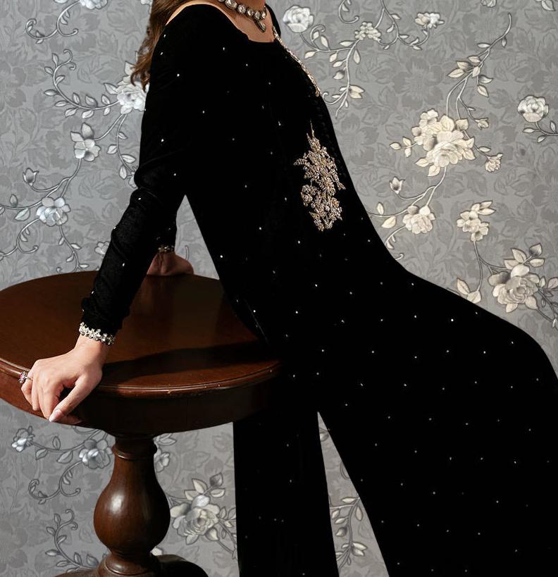 A woman in a black dress with a floral pattern stands in front of a gray floral wallpaper.