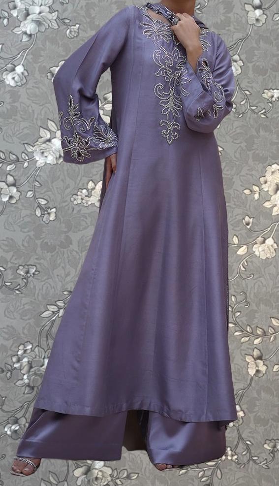 A person wearing a long, purple dress with intricate embroidered designs on the sleeves and hem.