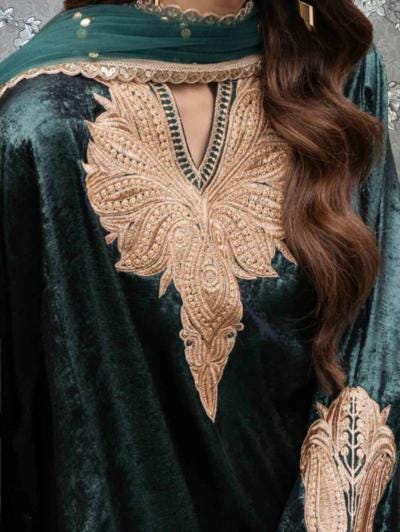 a close-up view of a woman's torso wearing a green velvet dress with intricate gold embroidery. The dress features a large, detailed embroidered design on the front, which is the focal point of the image.