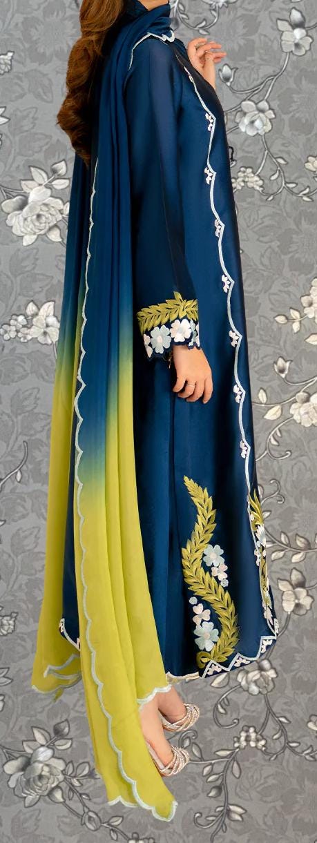 A person wearing a blue and yellow dress with intricate embroidered designs, standing against a gray floral background.