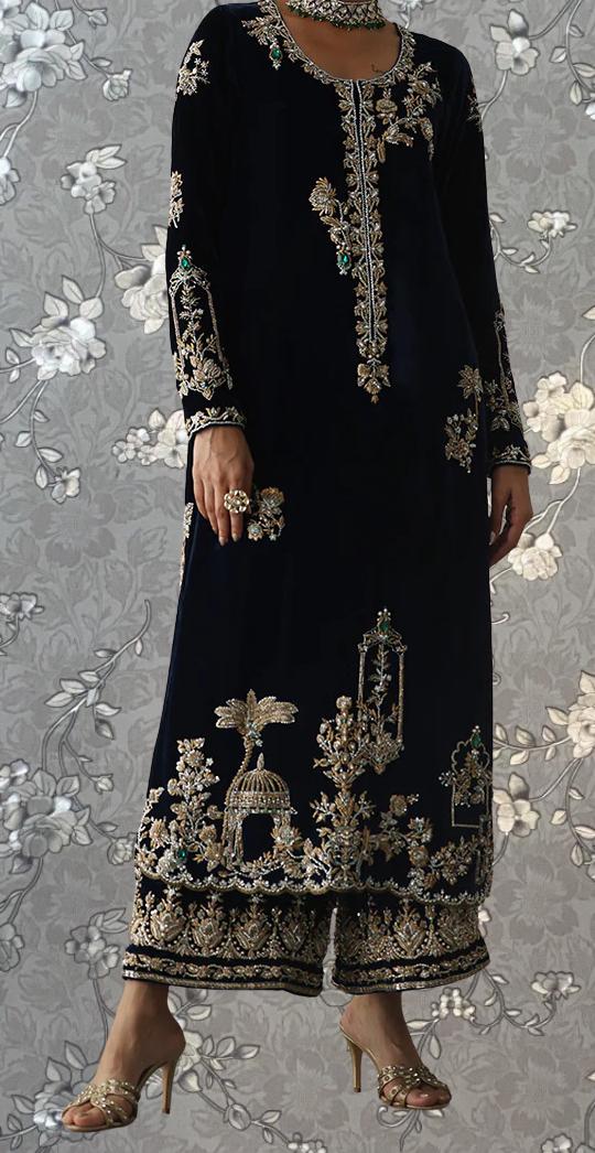 A person wearing a long, black dress with intricate gold embroidery and floral designs, standing against a gray floral background.