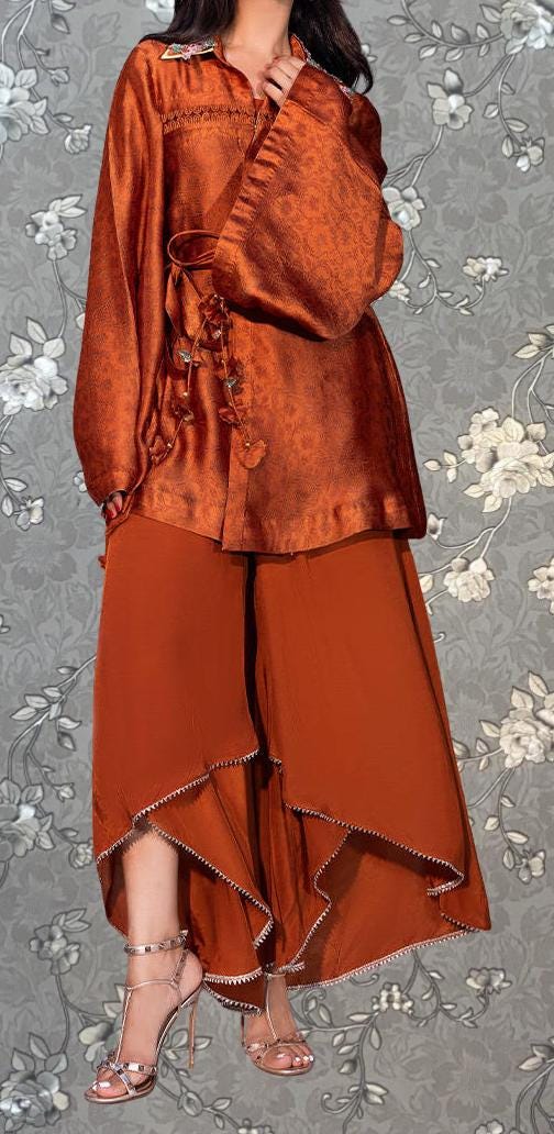 A woman wearing a long, orange dress with a high slit and a matching skirt, standing against a gray floral background.