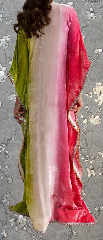 a person wearing a long, colorful dress with a gradient of colors, including green, pink, and white. The dress has a flowing, draped design and appears to be made of a soft, shiny fabric. The person is standing against a gray floral background, which complements the vibrant colors of the dress.