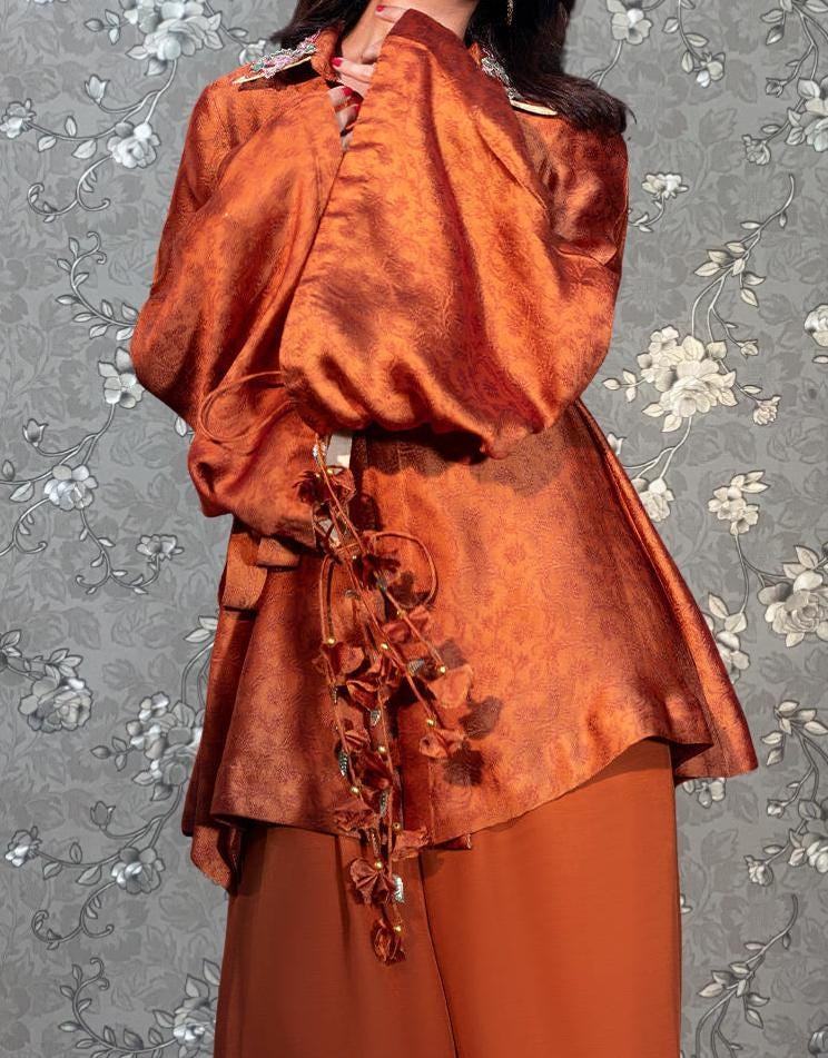 A person wearing a vibrant orange dress with a floral pattern and a long, flowing skirt.