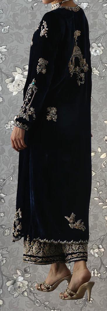 A person wearing a long, black velvet dress with intricate gold embroidery and a matching gold and white high-heeled shoe.