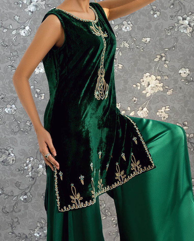 A woman wearing a green velvet dress with gold embroidery poses against a gray floral background.