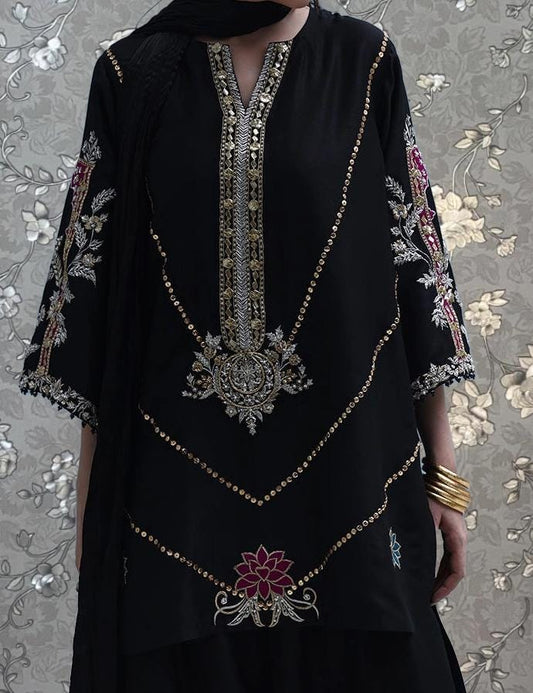 A person wearing a black dress with intricate gold embroidery and floral designs, standing against a floral patterned background.