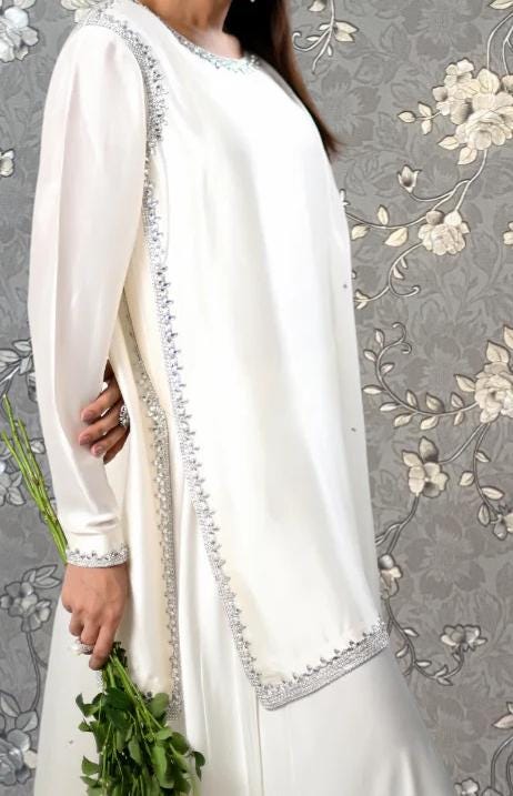 A woman wearing a white dress with a long train and holding a bunch of green flowers.