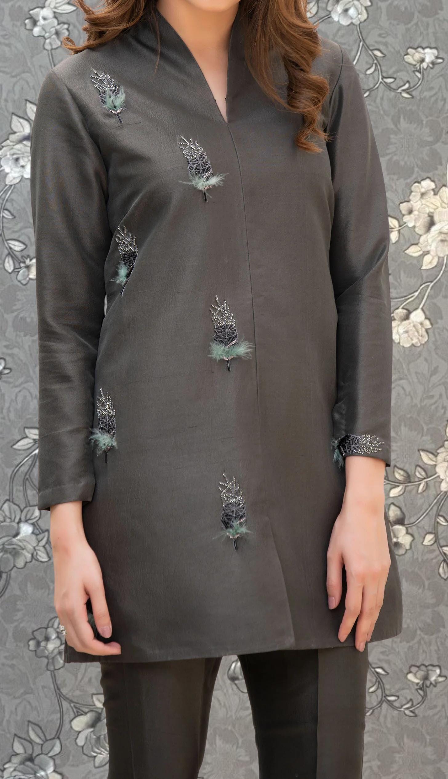 A woman wearing a gray dress with green floral embroidery on the front.