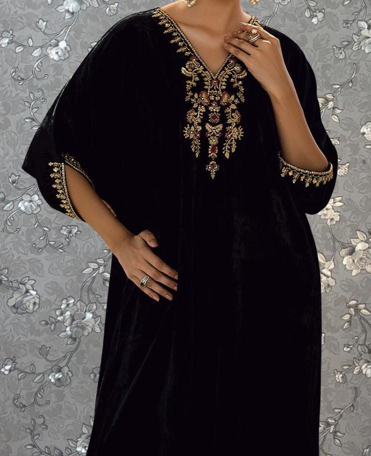 A person wearing a black velvet dress with gold embroidery and jewelry poses against a floral background.