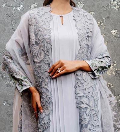 A woman wearing a gray dress with intricate floral embroidery and a matching gray shawl.