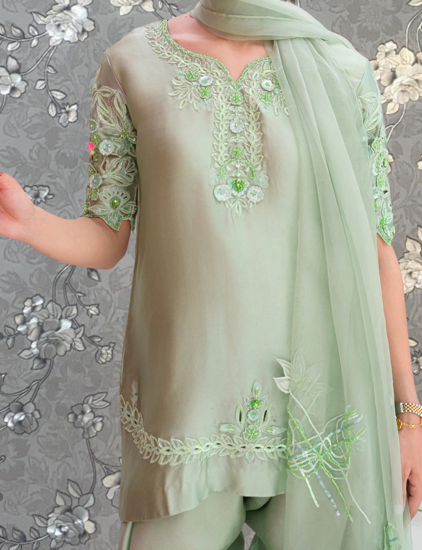 A person wearing a light green dress with intricate embroidery and a matching green scarf.