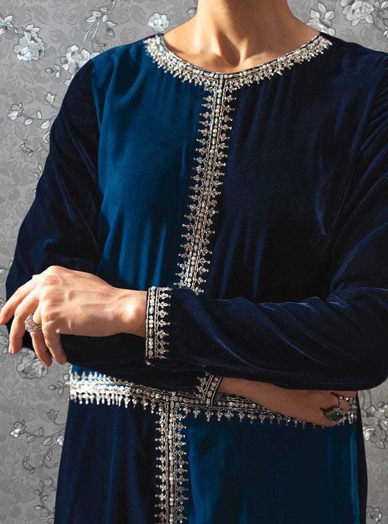 A person wearing a blue velvet dress with intricate silver embroidery on the neckline and sleeves.