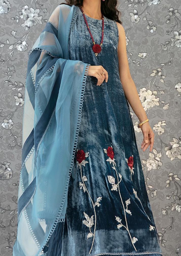 A woman wearing a blue velvet dress with red flowers and a matching blue shawl.