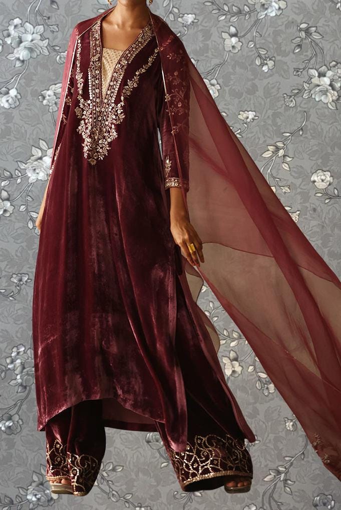 A woman wearing a long, burgundy velvet dress with intricate embroidery and a flowing red cape.