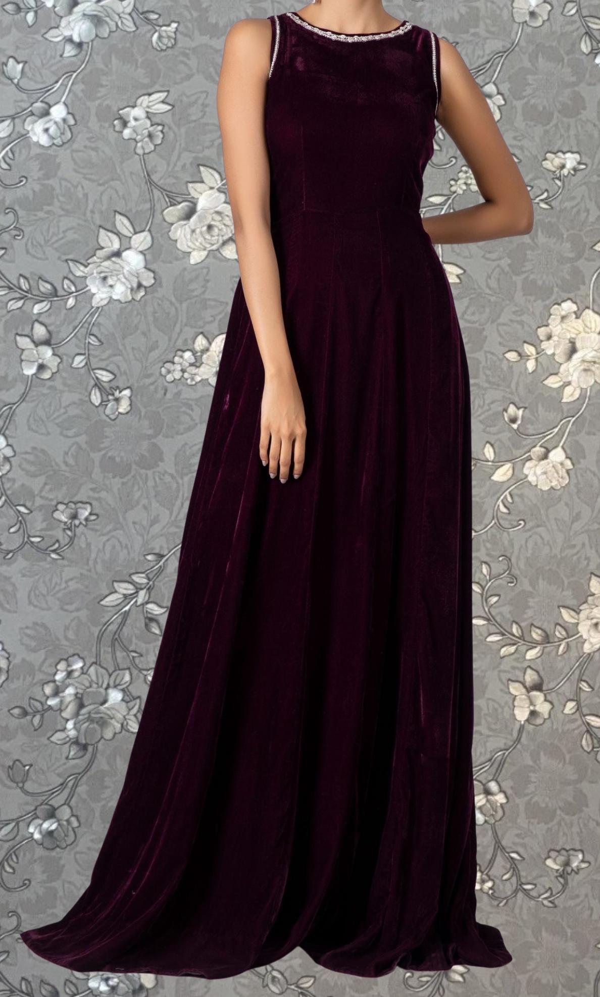 A woman wearing a long, burgundy velvet dress stands against a gray floral background.