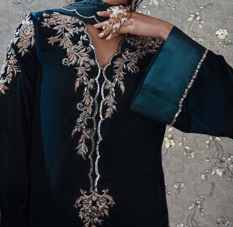 A close-up of a person wearing a dark blue dress with intricate embroidered patterns and a matching blue sleeve.