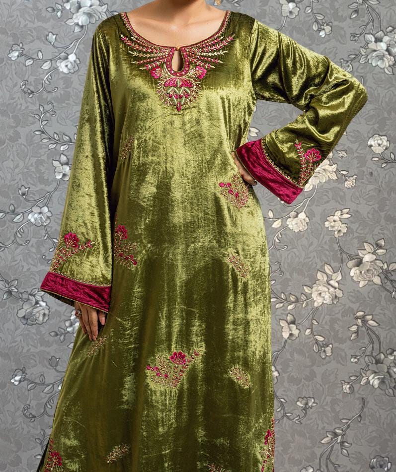 A woman wearing a long, green dress with pink floral embroidery on the sleeves and collar.
