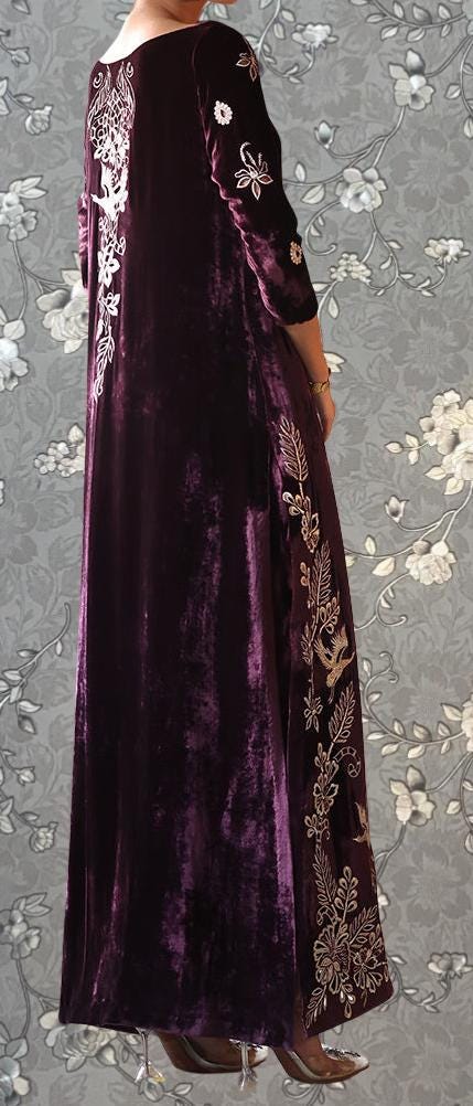 a person wearing a long, burgundy velvet dress with intricate embroidered designs on the sleeves and hem.