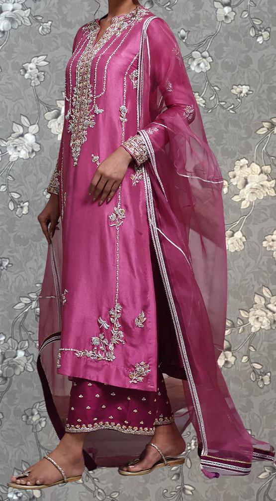 A woman wearing a long pink dress with intricate embroidery and a matching pink shawl.