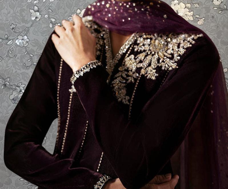 A close-up of a person wearing a dark purple dress with intricate embroidery and a matching headscarf.