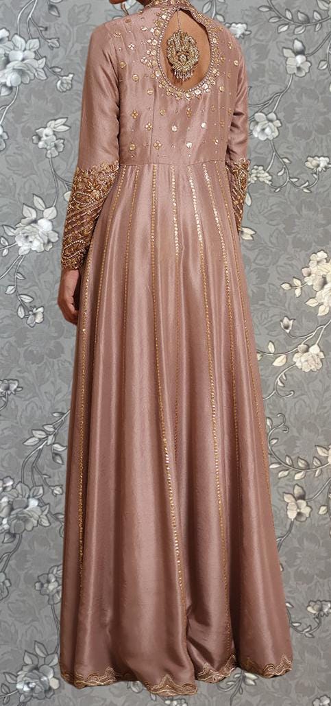A woman wearing a long, pink dress with gold embroidery and a large back opening.