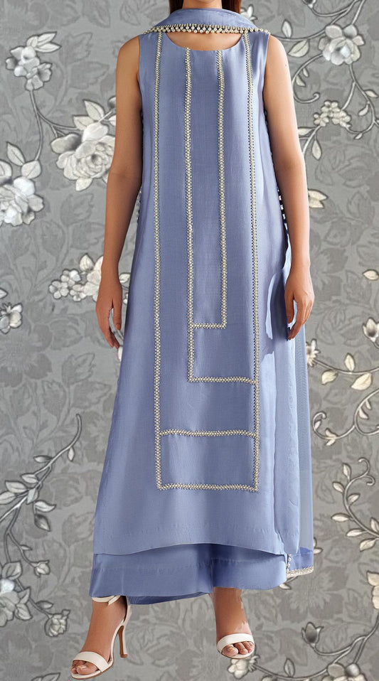 A woman wearing a sleeveless blue dress with a geometric pattern and white accents, standing against a gray floral background.