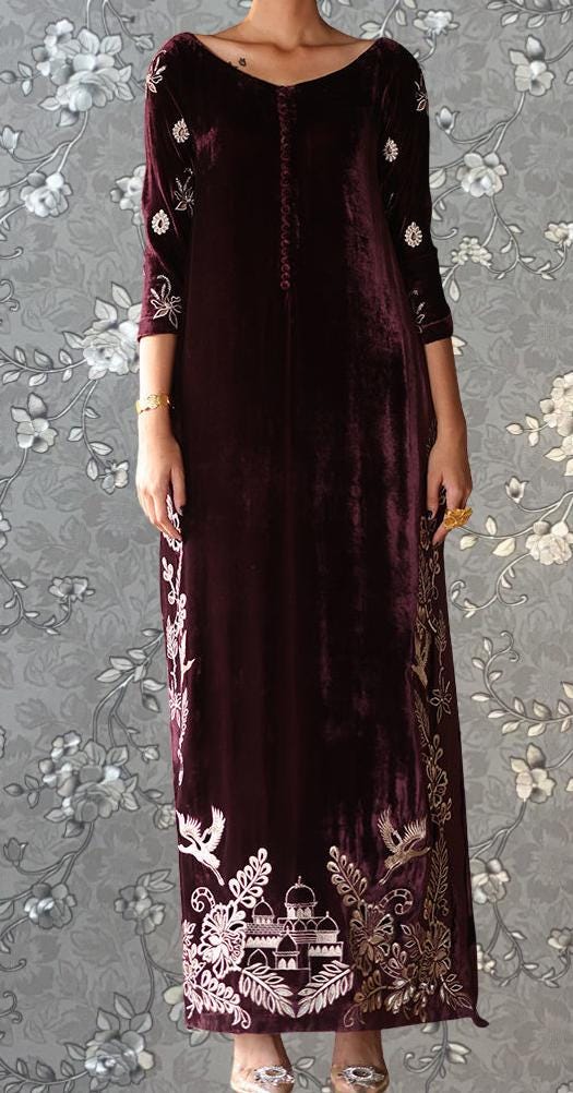 A woman wearing a long, burgundy velvet dress with intricate embroidered designs on the front.