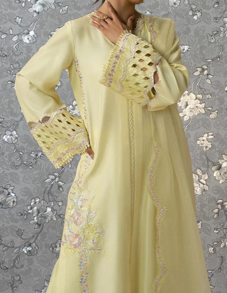 A woman wearing a long, yellow dress with intricate embroidered designs on the sleeves and hem.