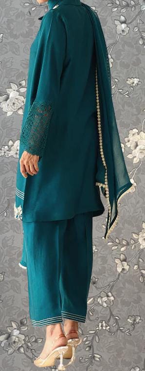 A person wearing a teal-colored outfit with lace sleeves and a matching skirt, standing against a gray floral background.