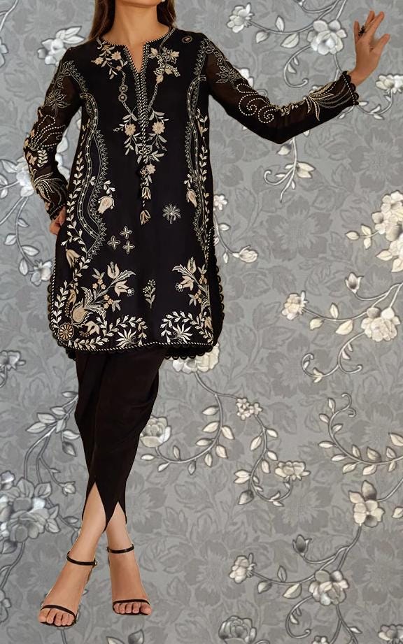 A woman wearing a black dress with intricate floral embroidery poses against a gray floral background.