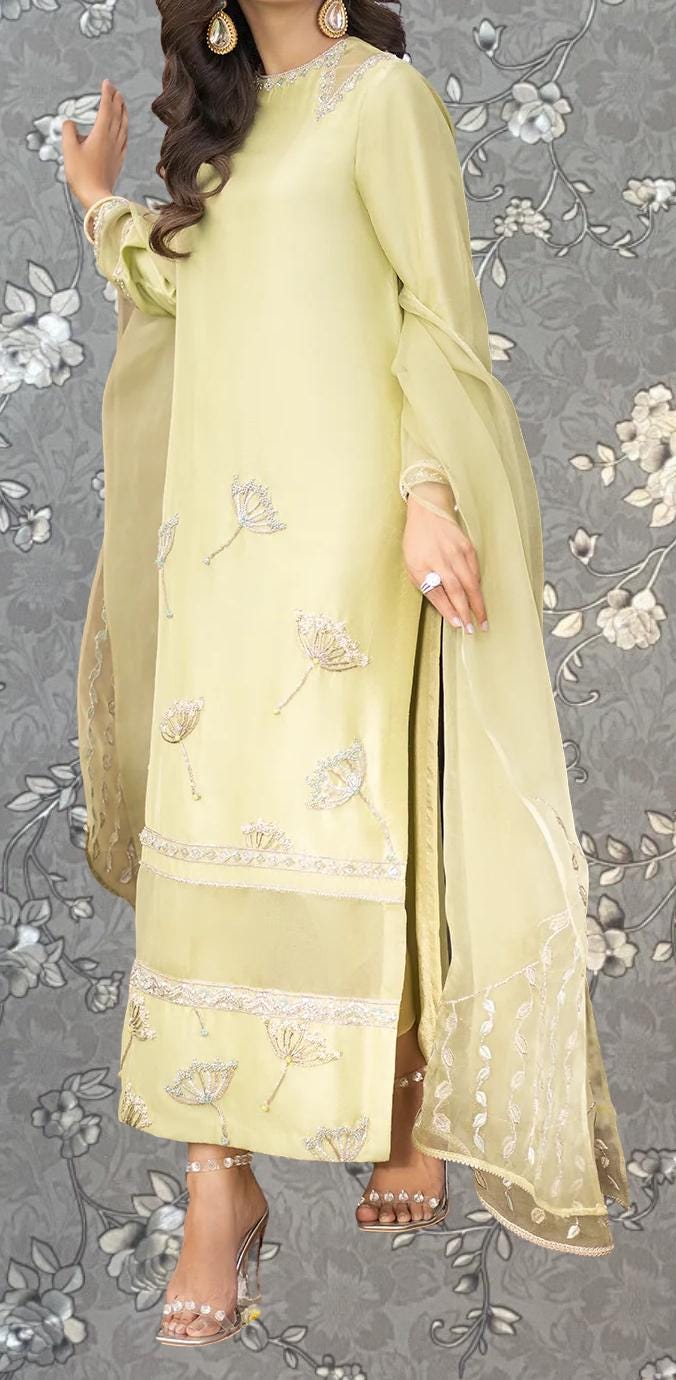 A woman wearing a yellow dress with intricate embroidery poses against a gray floral background.