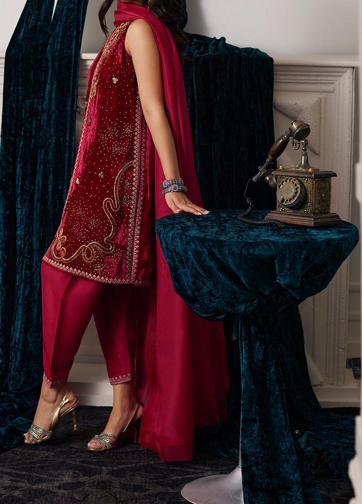 A woman in a red and gold dress stands next to a vintage-style telephone, with a blue velvet tablecloth and gold shoes visible in the background.