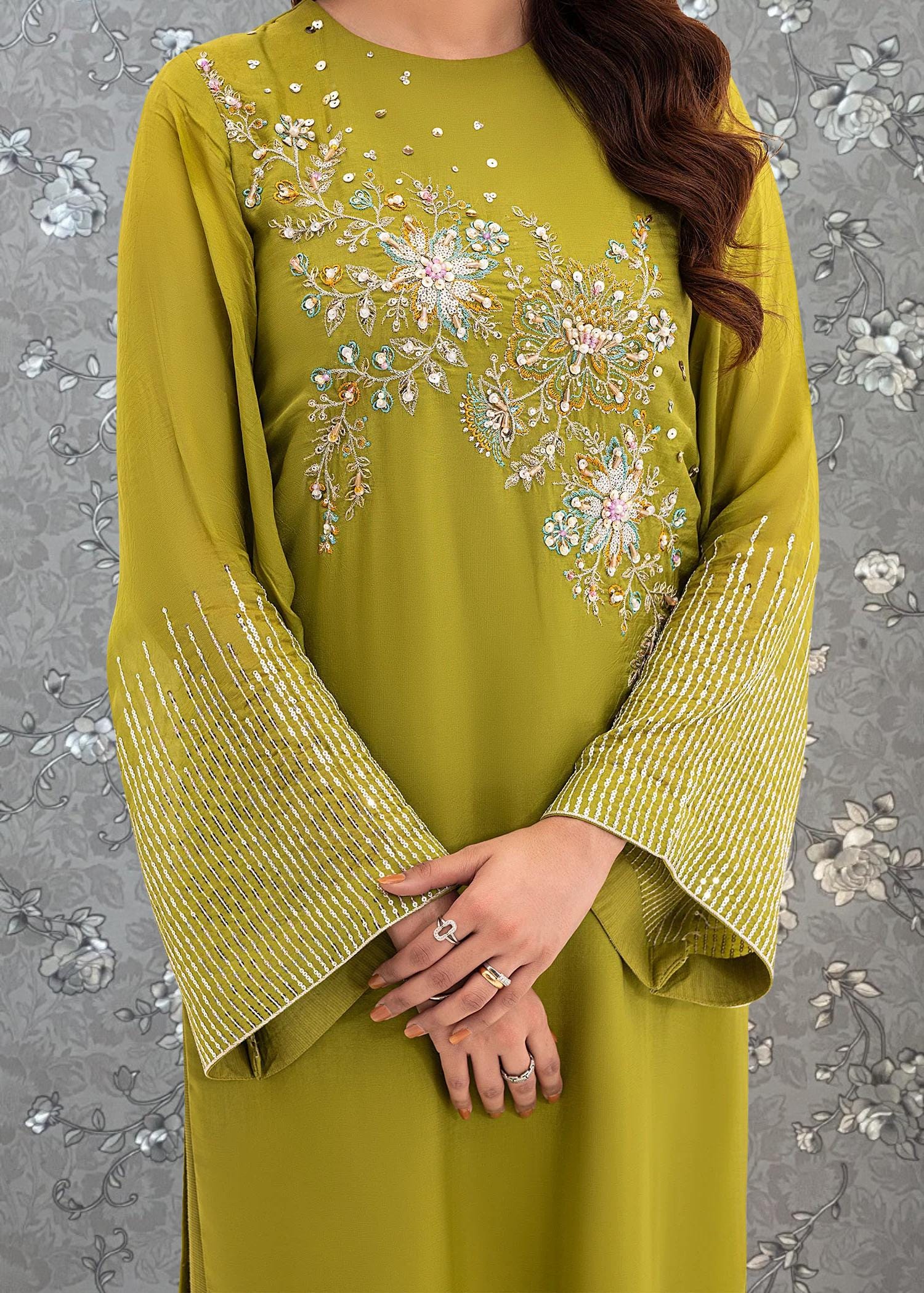 A woman wearing a vibrant green dress with intricate floral embroidery on the sleeves and neckline.