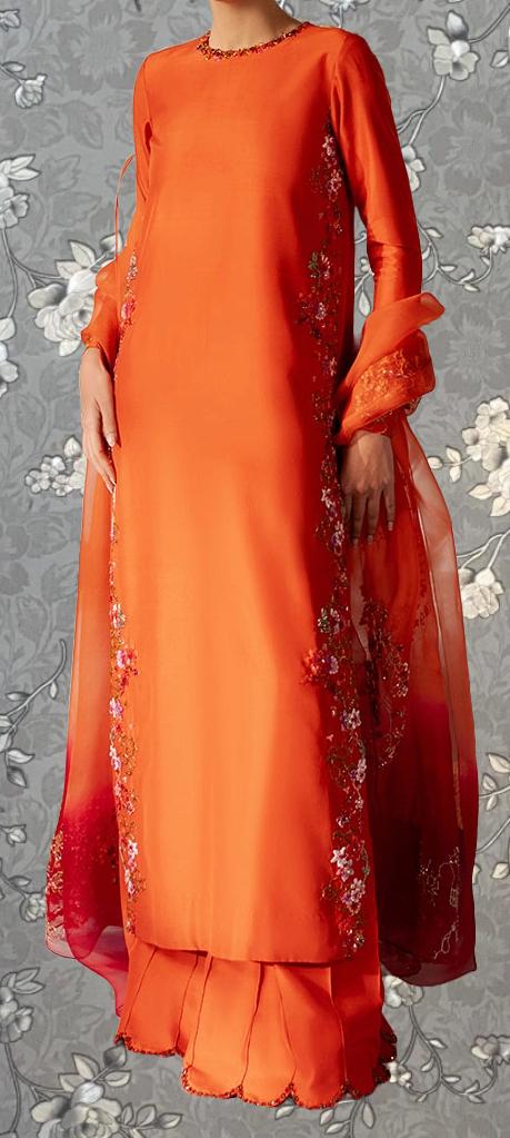 A person wearing a long, orange dress with floral embroidery on the sleeves and skirt.