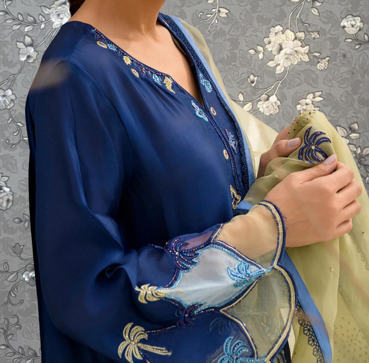 A close-up of a person wearing a blue dress with intricate embroidery and a matching blue shawl.