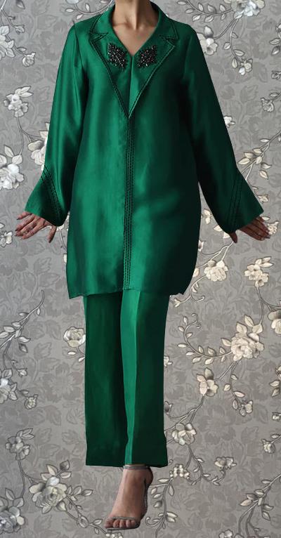 A person wearing a green jacket with a floral pattern and matching green pants stands against a gray floral background.