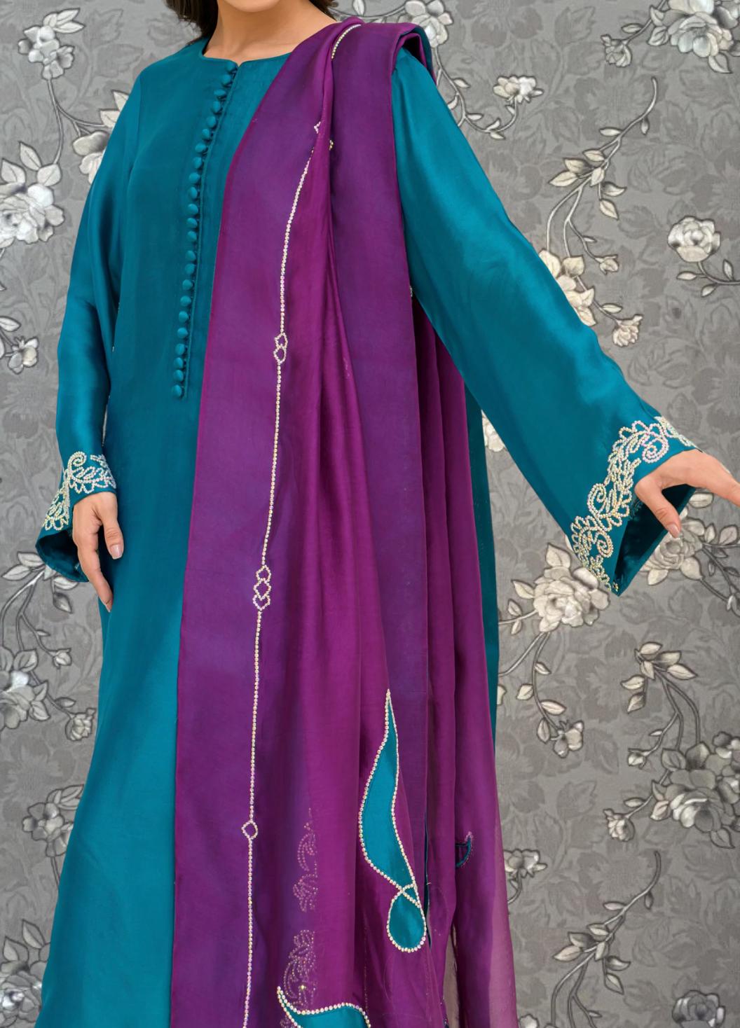A woman wearing a long, teal-colored dress with a purple shawl draped over her shoulders.