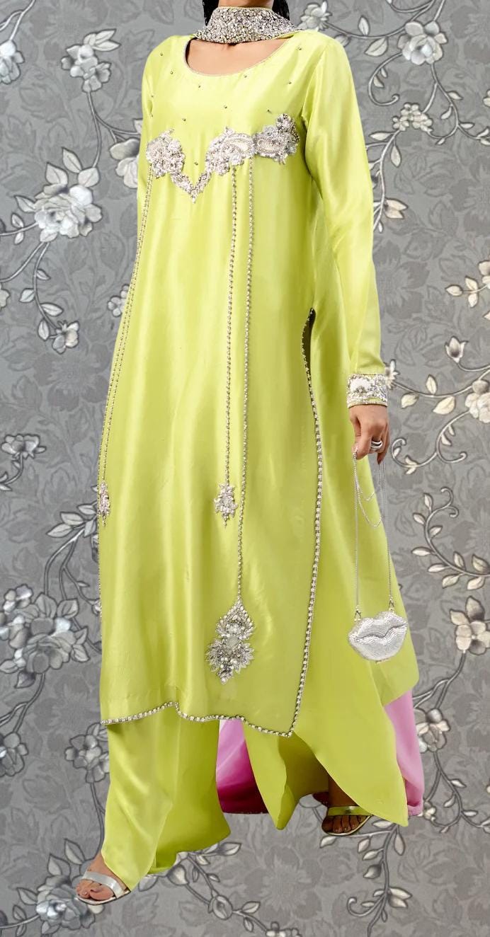 A woman wearing a bright yellow dress with intricate beading and embroidery, standing against a gray floral background.