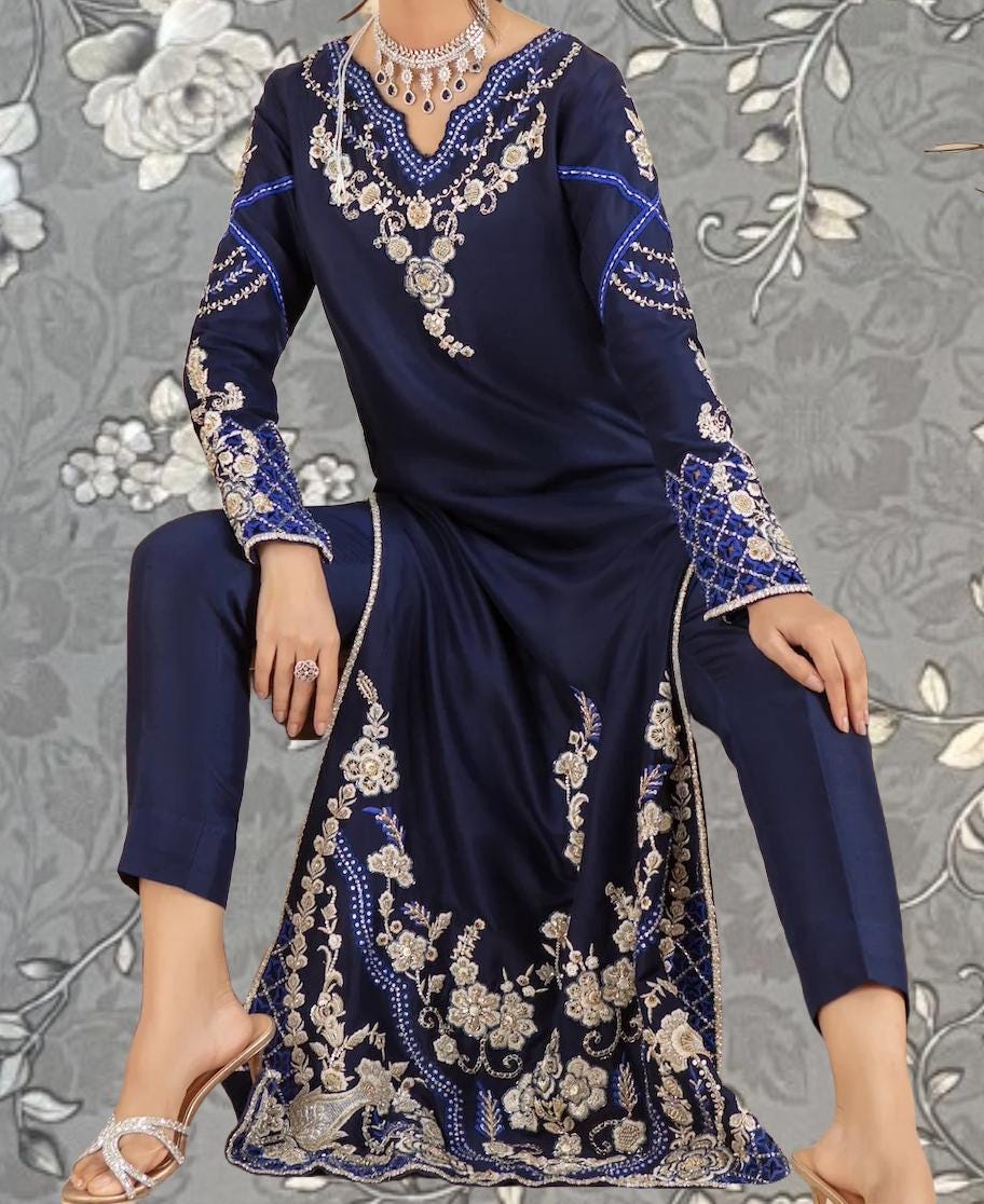 A woman wearing a long navy blue dress with intricate gold embroidery and a matching necklace.