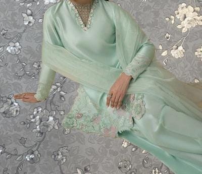 A woman wearing a mint green dress with lace detailing and a matching mint green scarf is shown against a gray floral background.