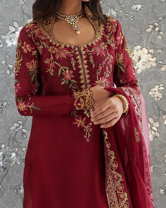 A woman wearing a red and gold embroidered dress with a matching necklace and bracelet.