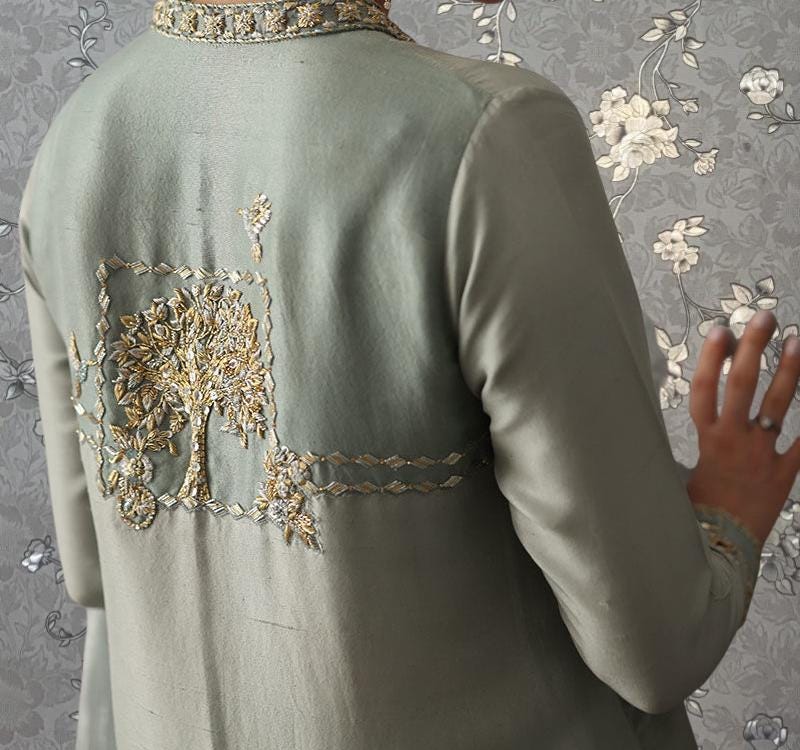 a close-up view of a person's back, wearing a grey jacket with intricate embroidered designs.