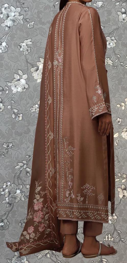 a person wearing a long, brown dress with intricate embroidered patterns. The dress has a long train and a high collar, giving it a formal and elegant appearance. The person is standing against a gray floral background, which complements the overall color and design of the dress.