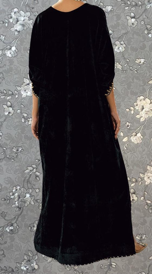 A person wearing a long black dress with gold accents, standing against a gray floral background.