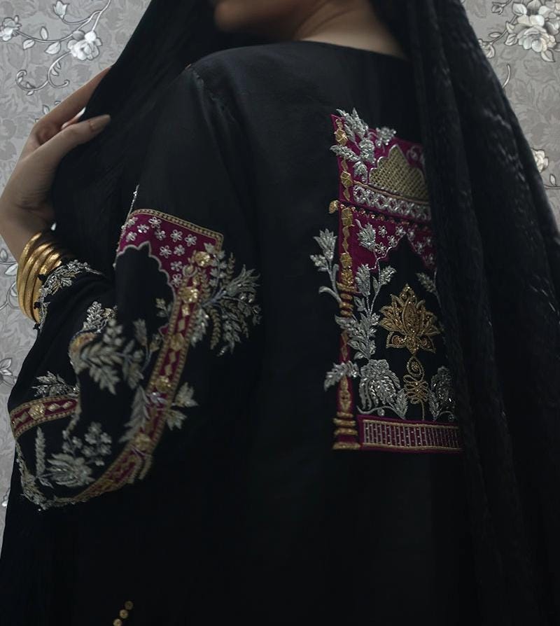 a person wearing a black dress with intricate embroidered designs on the sleeves and back.