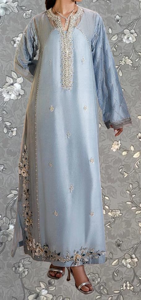 A woman wearing a long, light blue dress with intricate embroidery and floral patterns.